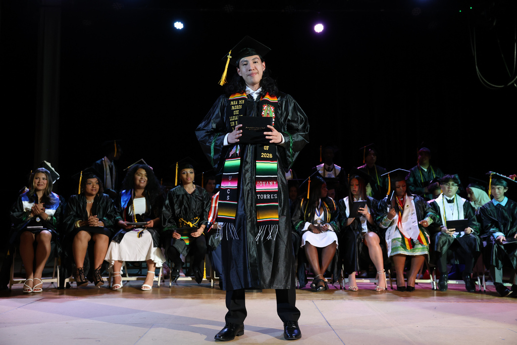 A student shows off their diploma while standing on stage at high school graduation.