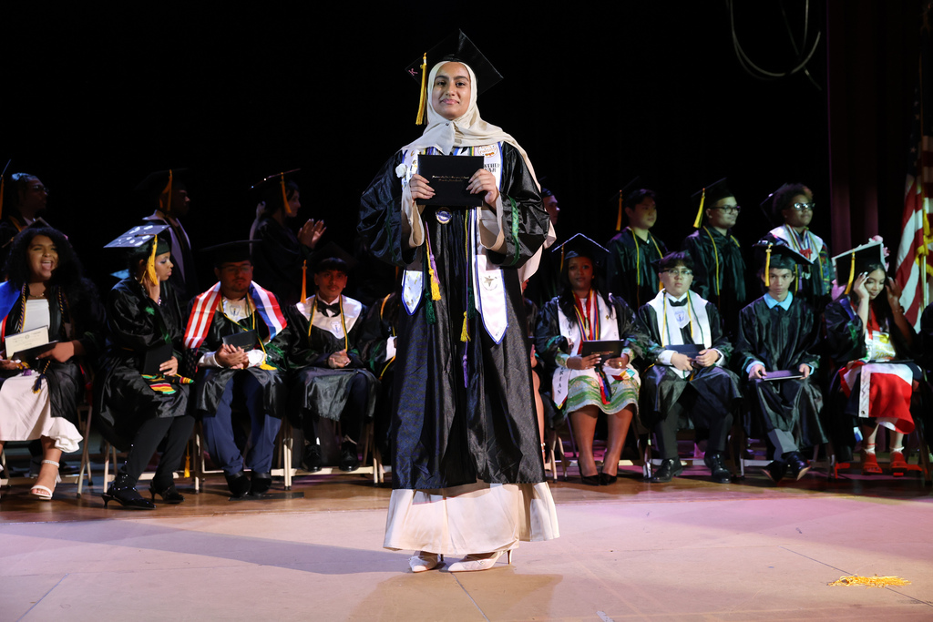 A student holds their diploma while walking across stage at high school graduation.