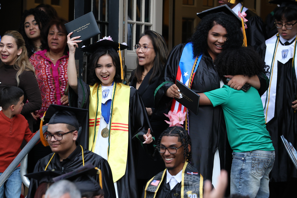 A student raises their diploma while walking through a crowd of people.