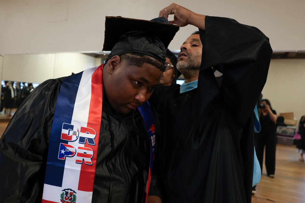 A student gets help with their graduation cap from a teacher before a high school graduation.