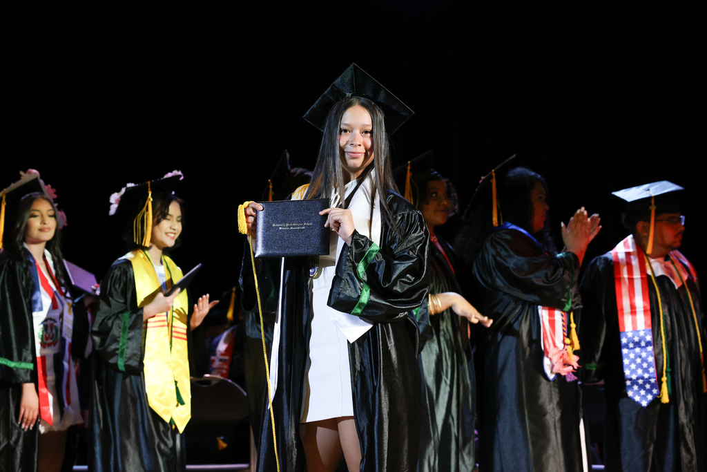 A student holds their diploma up while walking across the stage and their high school graduation.