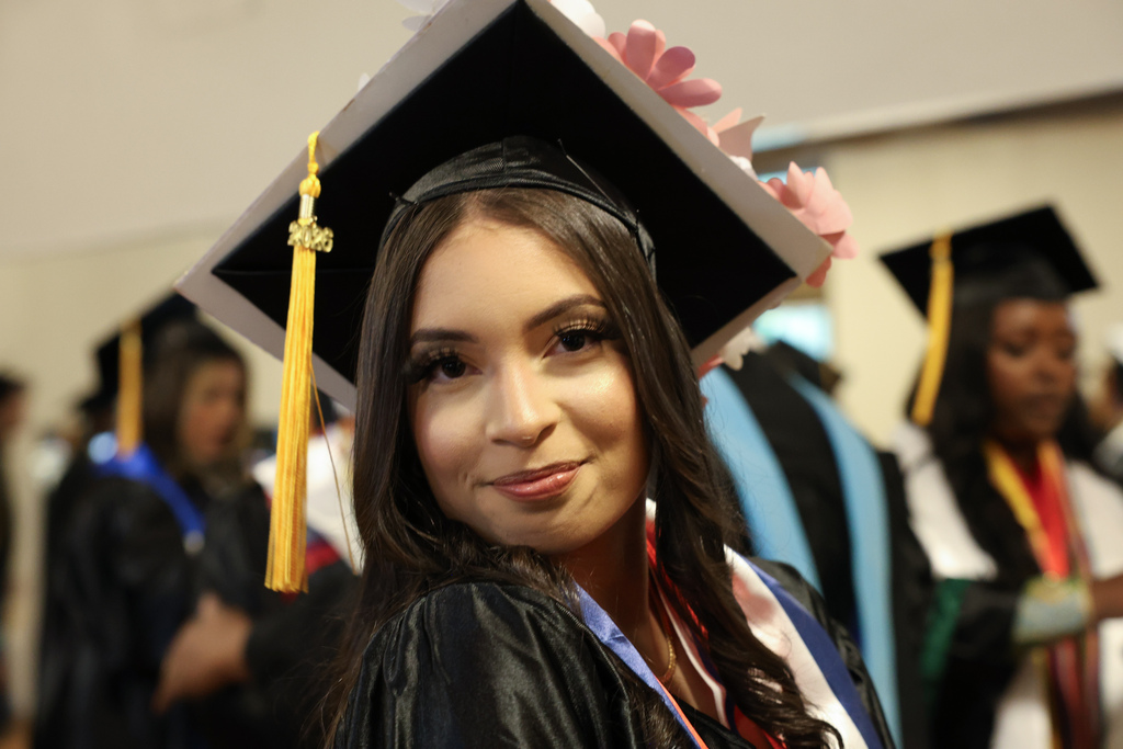 A student wearing a graduation cap and gown smiles.