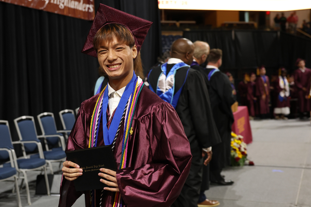 A student smiles while walking off stage at their high school graduation, holding their diploma. 
