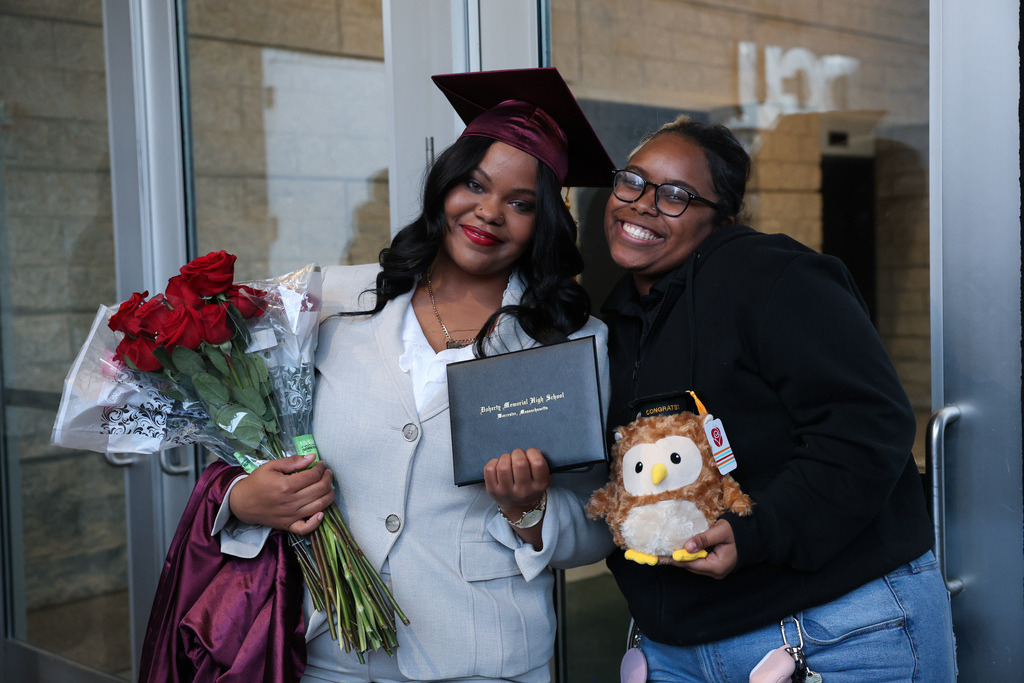 A student stands alongside a family member while holding their high school diploma.