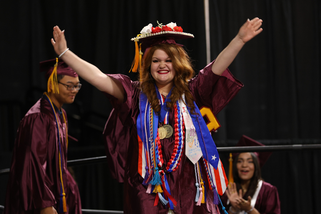 A student raises their arms in celebration while walking across stage at their high school graduation.