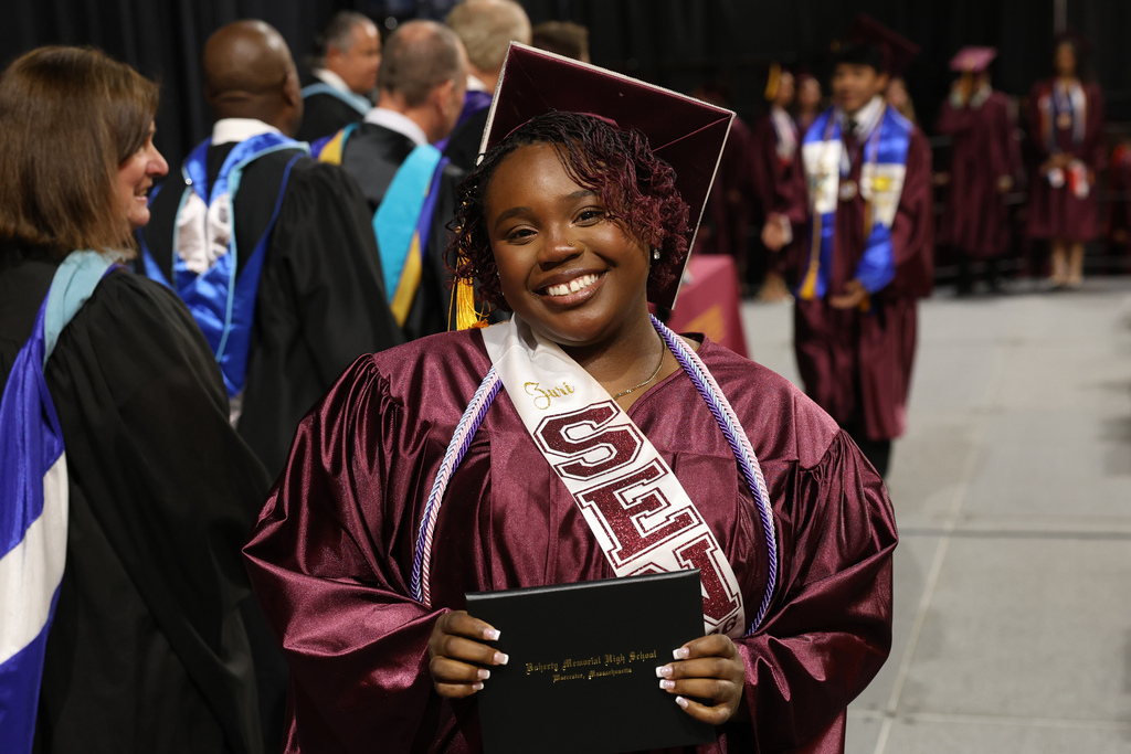 A student smiles while walking on stage at their high school graduation.