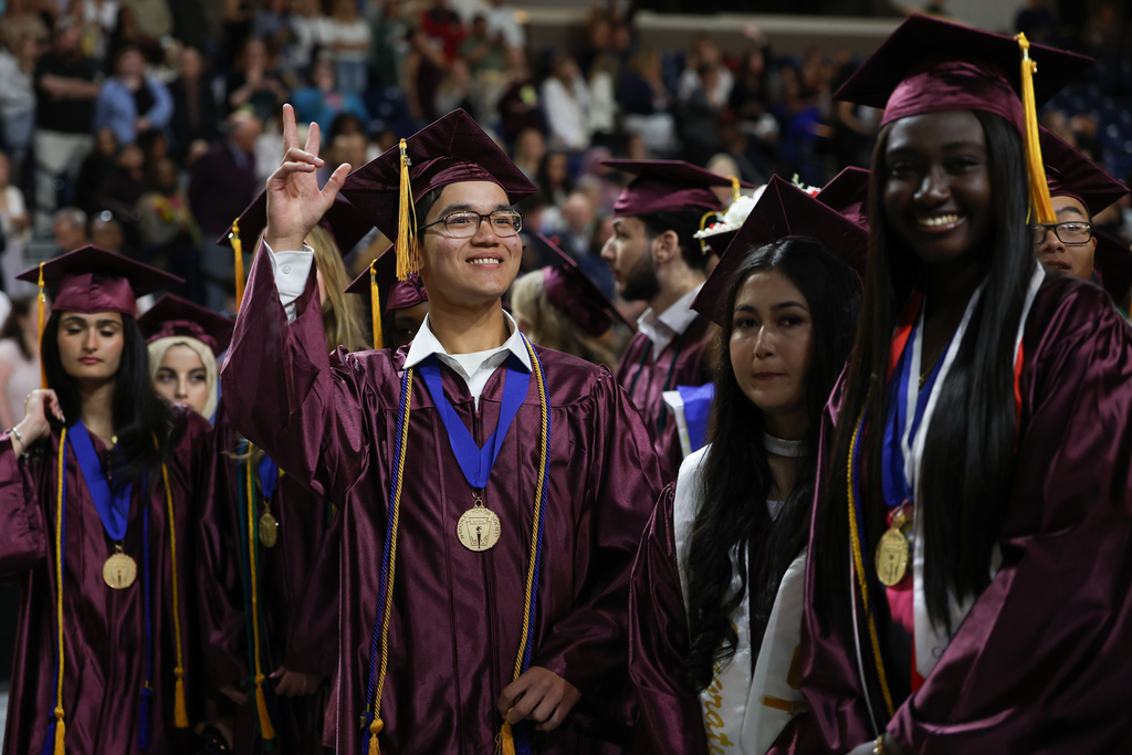 A student wearing a graduation cap and gown waves to the crowd.