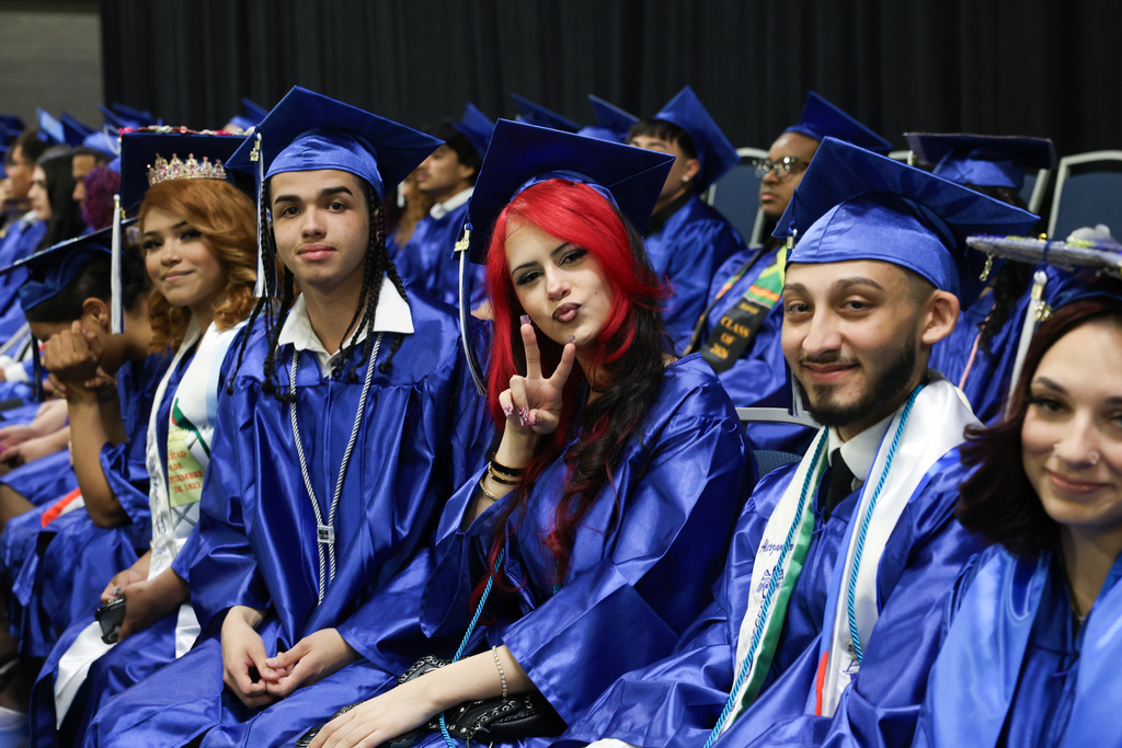 A student gives the peace sign while sitting in their row at graduation amongst classmates.