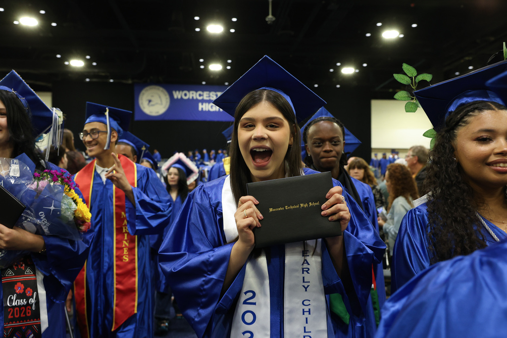 A student holds up their diploma with excitement as they walk off stage at graduation.