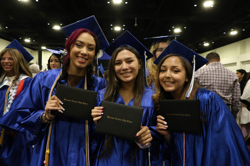 Three students wearing caps and gowns hold up their high school diplomas following graduation.