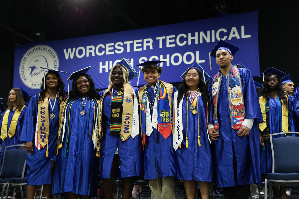 Six students stand side-by-side wearing graduation caps and gowns while a banner hangs overhead reading "Worcester Technical High School."