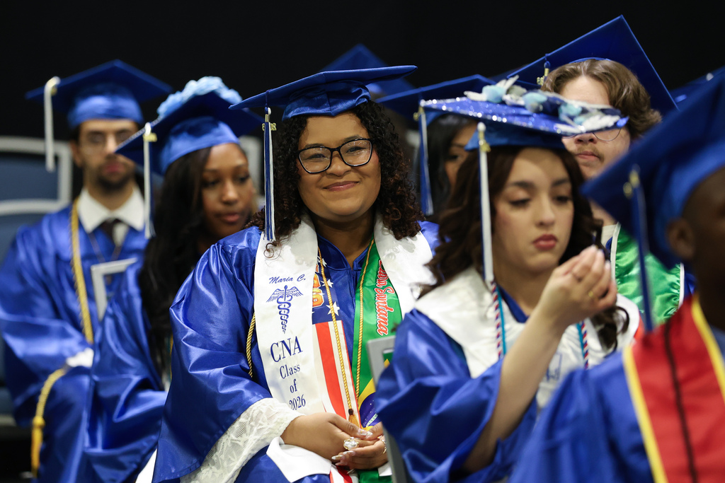 A student smiles in their seat while wearing a cap and gown at high school graduation.