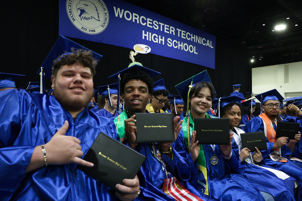 A row of students wearing caps and gowns hold up their high school diplomas following graduation.