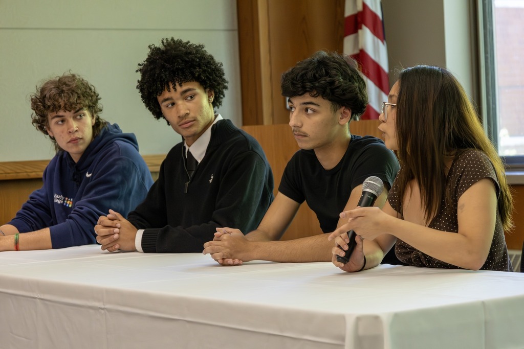 Four young people sit at a table, with one speaking into a microphone.