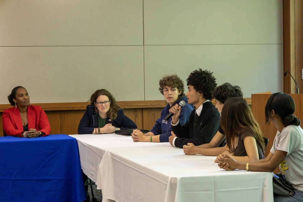A panel discussion with adults and young people seated at a long table.