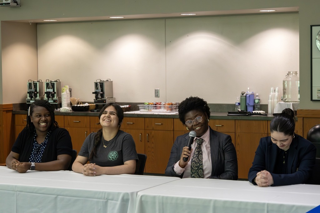 Four individuals sit at a table, with one speaking into a microphone.