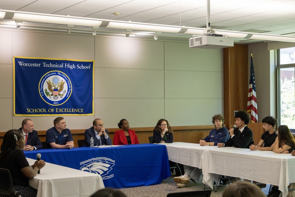 A panel discussion with adults and young people seated at a long table.