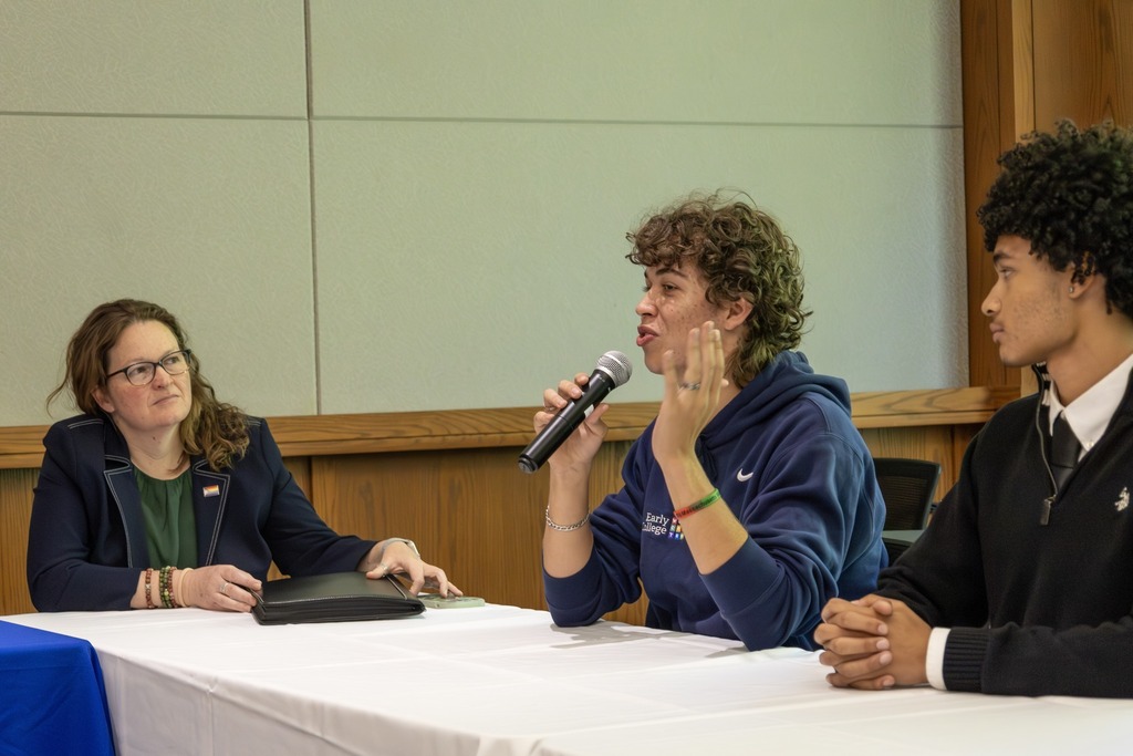 Three people sit at a table, with one speaking into a microphone.