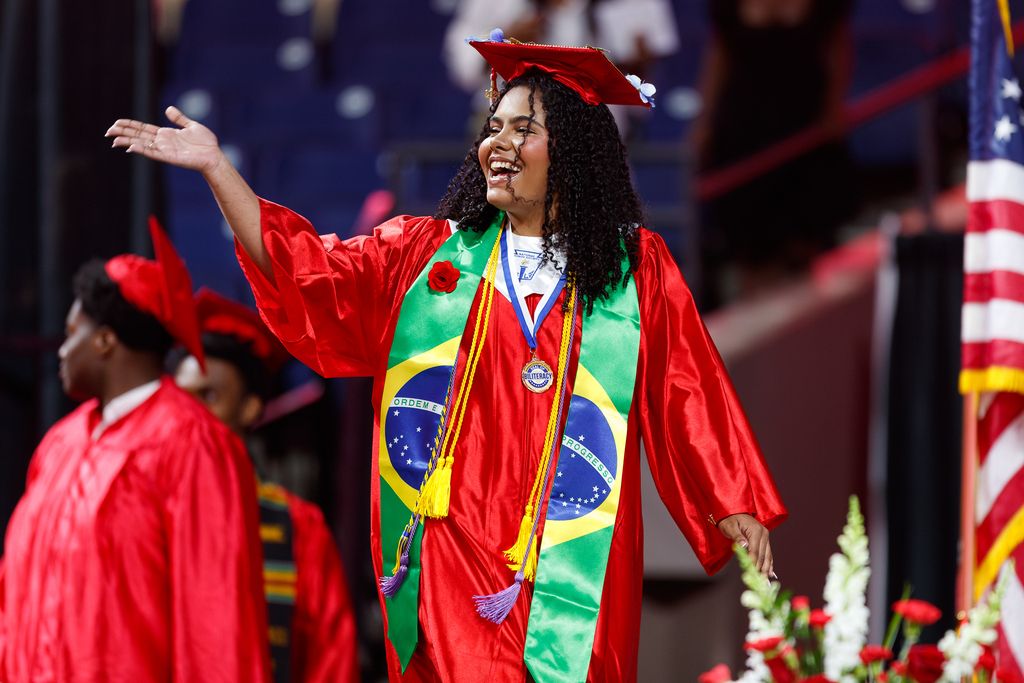 A student gestures to the crowd while walking the stage during high school graduation.