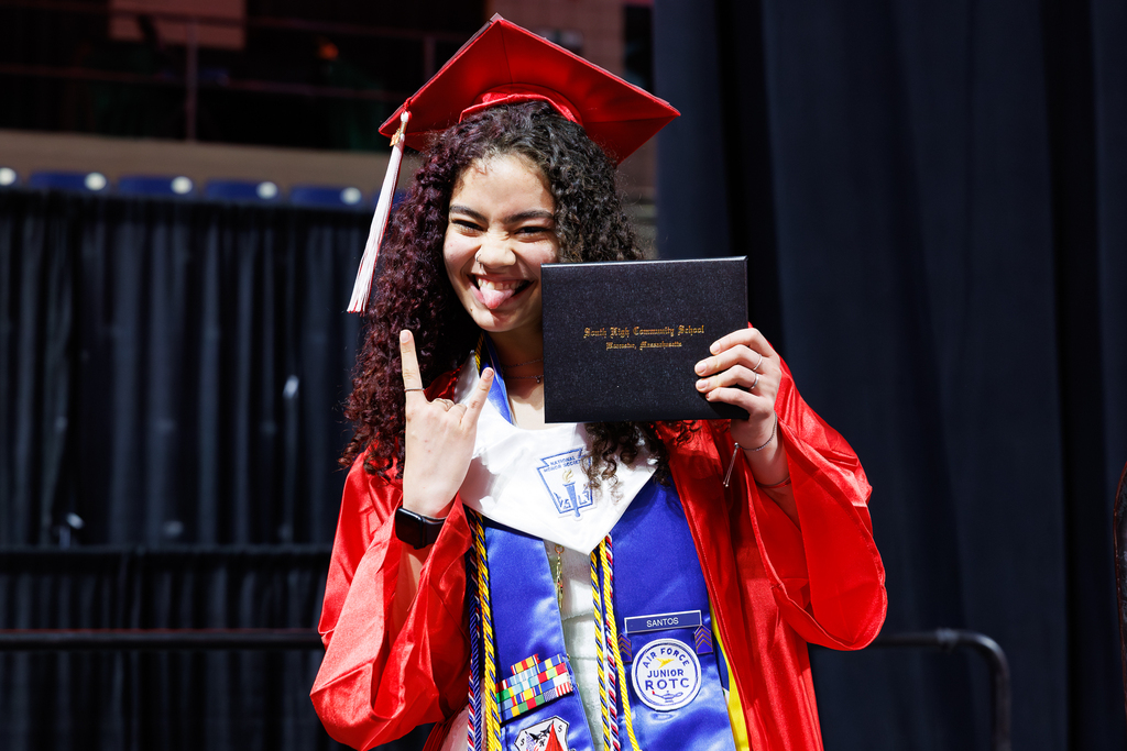 A high school student holds their diploma close to their face while sticking out their tongue.