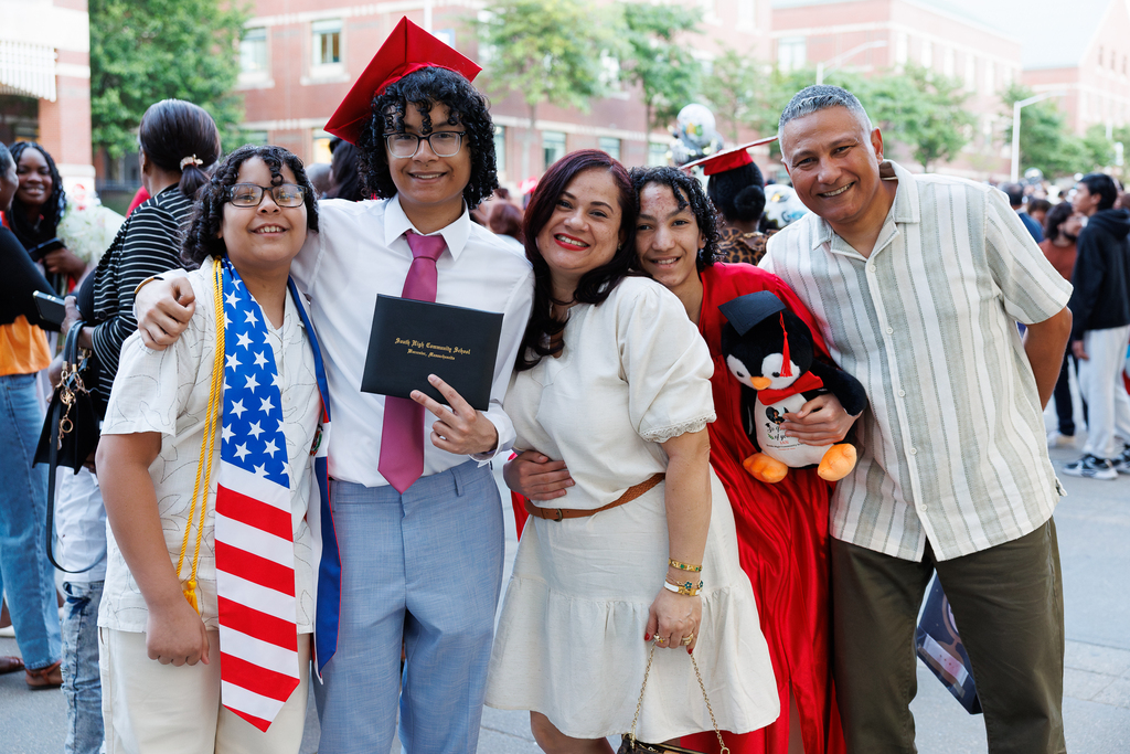 A family of five stand together following a high school graduation, each one wearing a different piece of graduation attire.