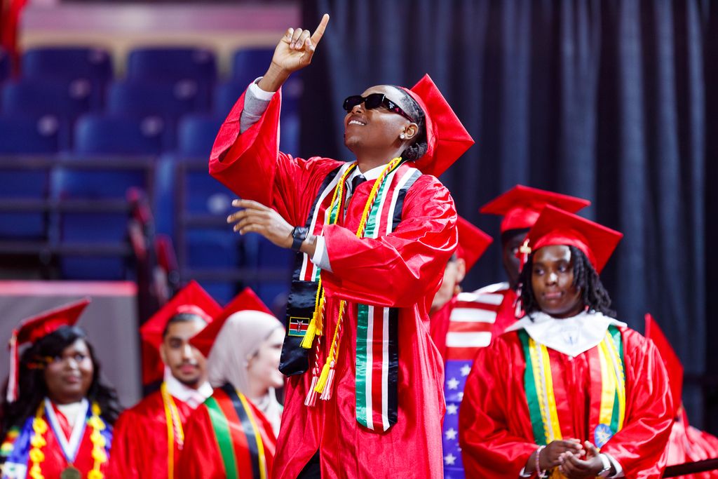 A high school student points to the sky as they walk the stage during high school graduation.