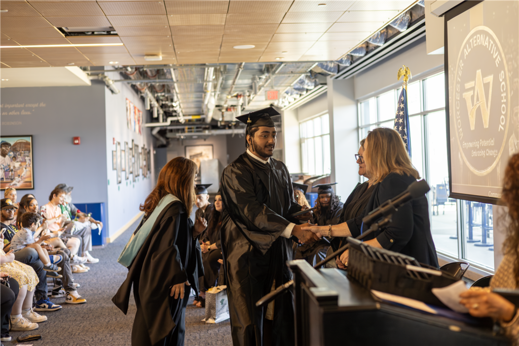 A graduate in a cap and gown shakes hands with an official at a graduation ceremony.