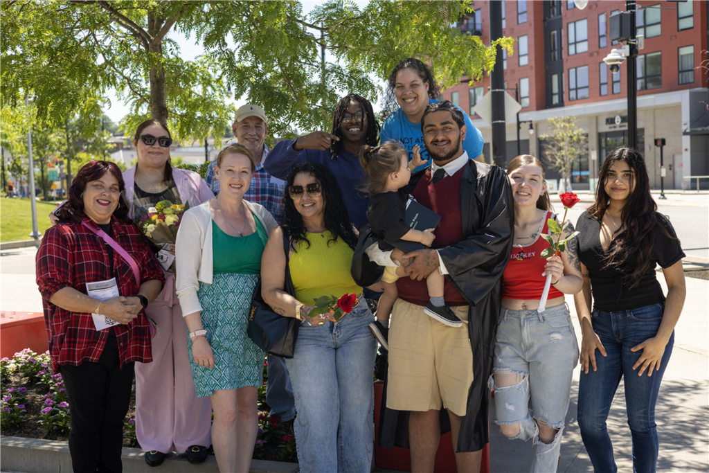 A diverse group of people, including a graduate in a cap and gown, pose for a photo outdoors.