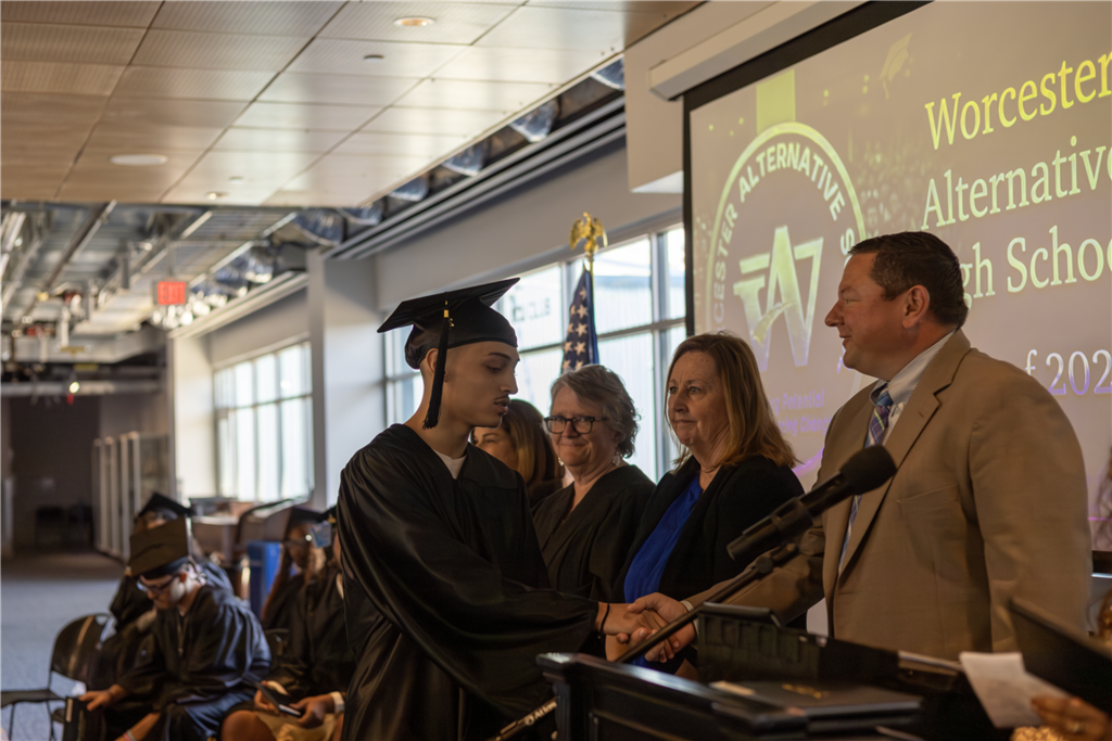 A graduate in a cap and gown shakes hands with an official at a ceremony.
