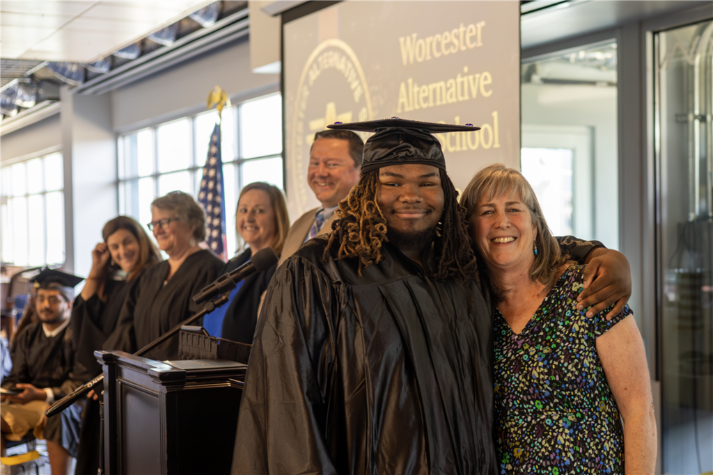 A graduate in a cap and gown smiles with a woman at a ceremony.