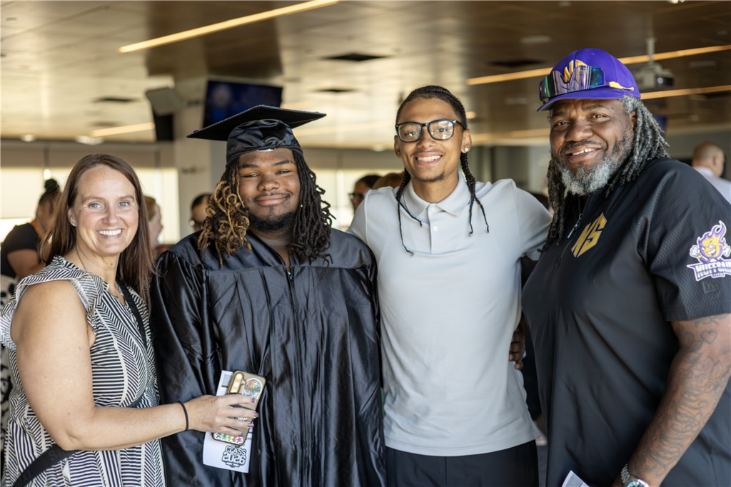 A graduating student in a cap and gown smiles with family members.
