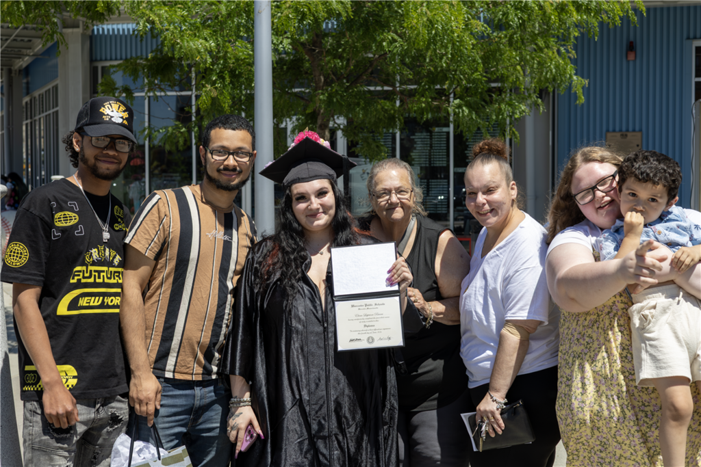 A group of people, including a graduate in a cap and gown, pose for a photo outdoors.