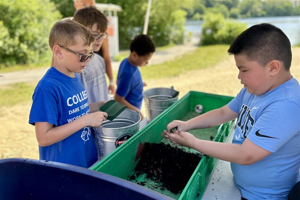 Children examine soil and small creatures in a green bin outdoors.