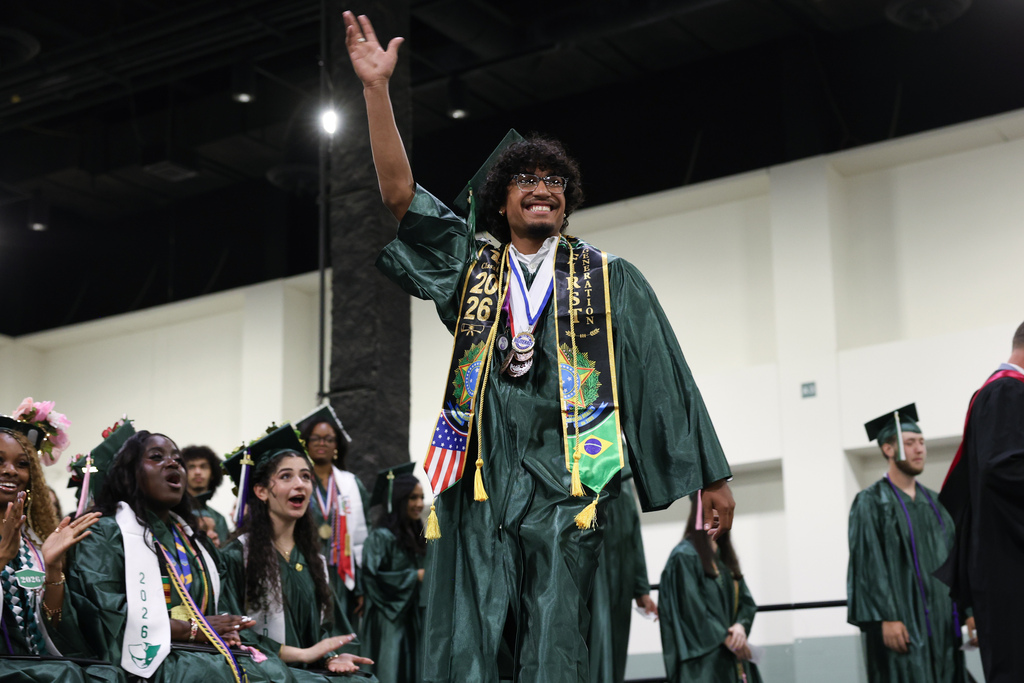 A student raises their hand in celebration as they walk across the stage at graduation.