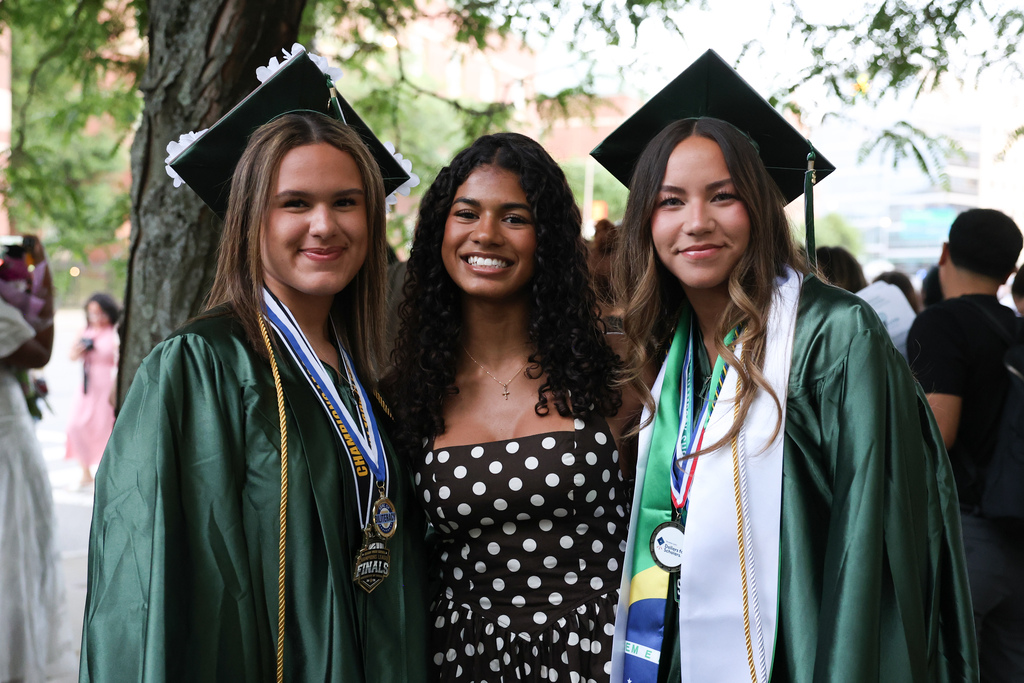Two high school graduates stand alongside a friend following graduation.