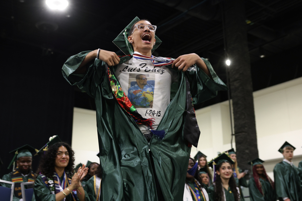 A student opens their graduation robe to reveal a shirt in honor of a family member during graduation.