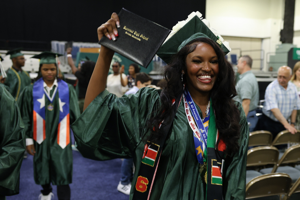 A student holds up their diploma while walking off stage.
