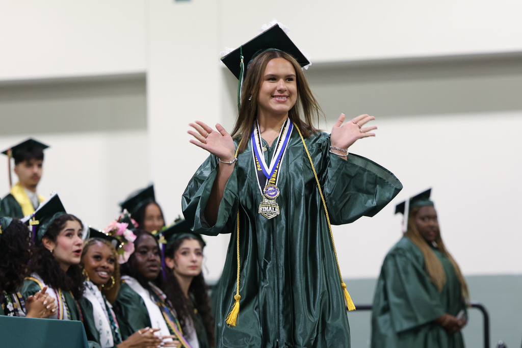 A student waves to the crowd as they walk the stage at graduation.