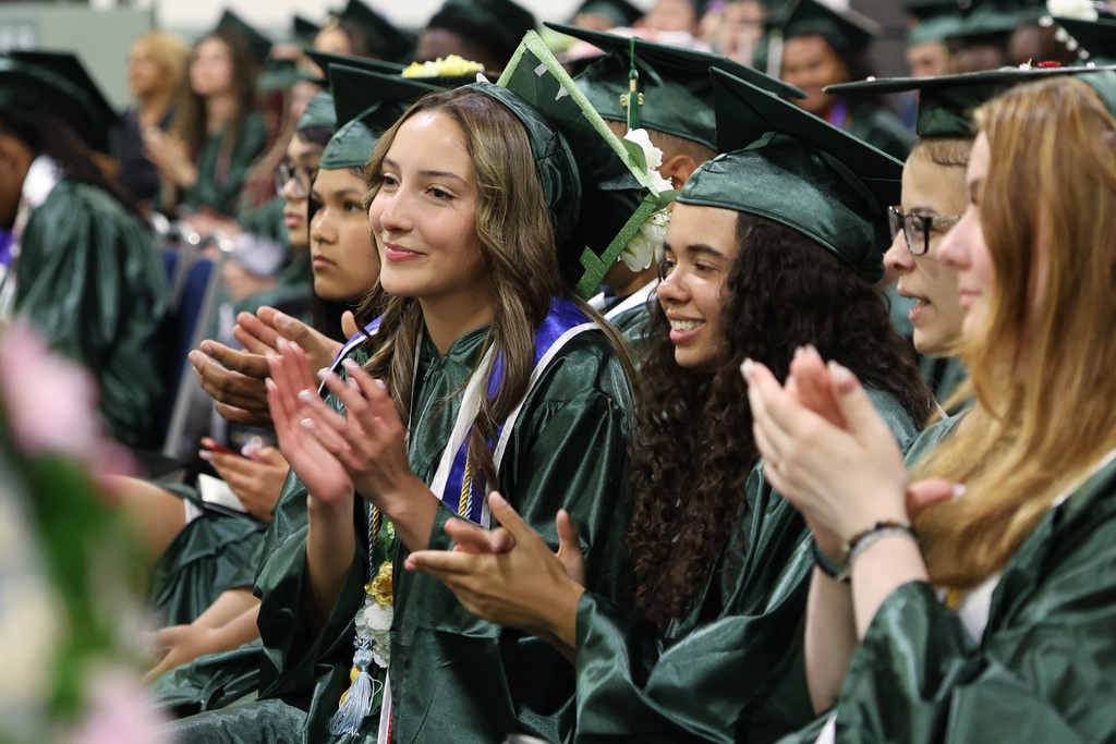 High school students cheer while seated during graduation.