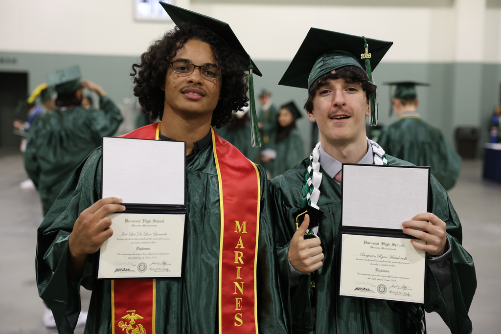 Two high school school graduates hold up their diplomas.
