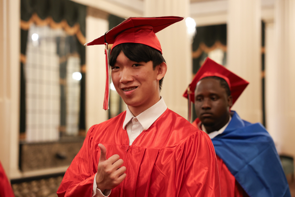 A high school graduate wearing a graduation cap gives a thumbs up.