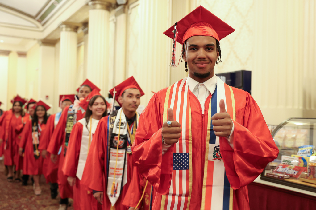A student wearing a graduation cap and gown gives two thumbs up.
