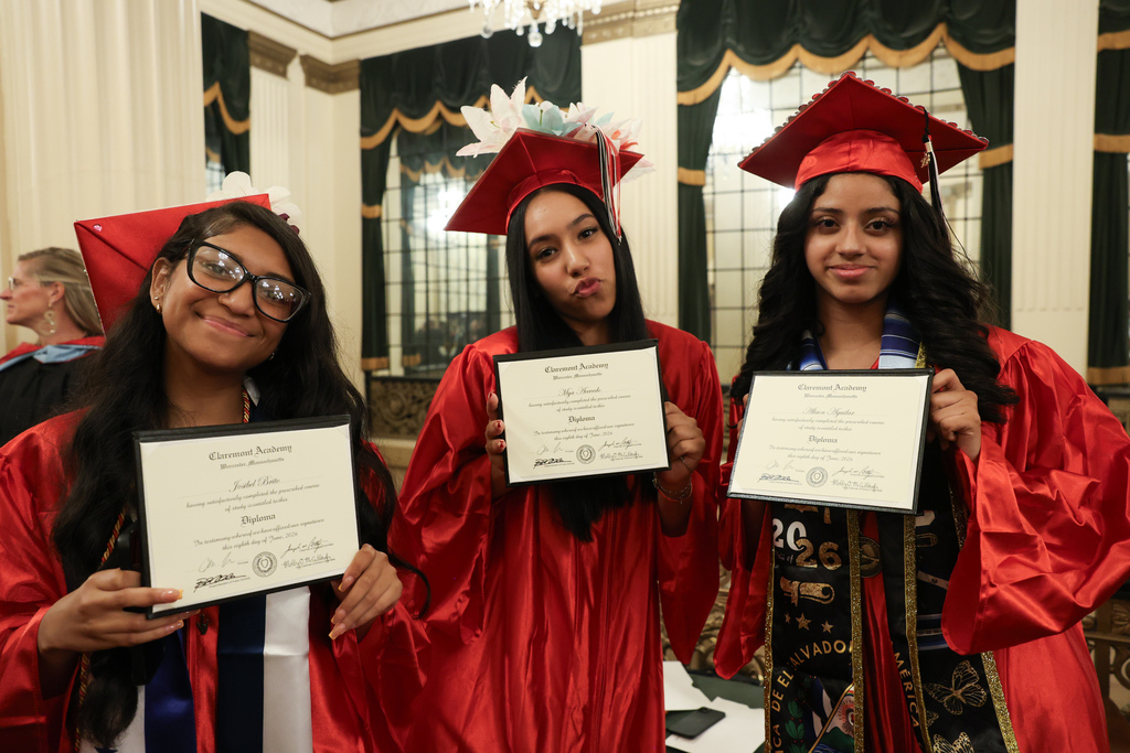 Three high school graduates stand side-by-side while holding their diplomas.
