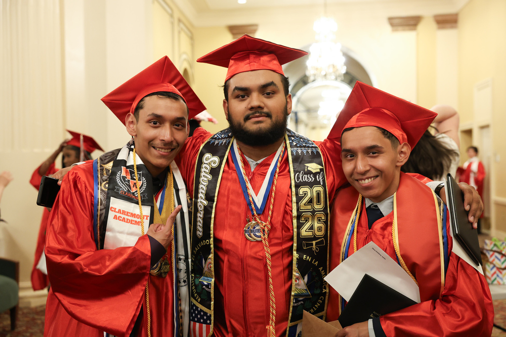 Three high school graduates hold up their diplomas while wearing caps and gowns.