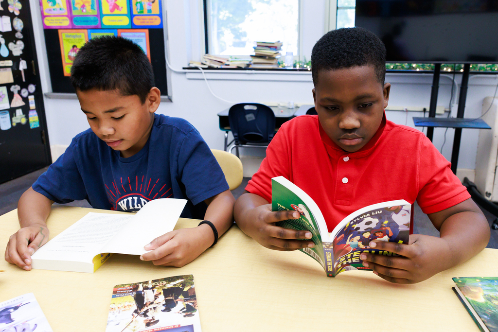 Two students read while sitting at their chairs.