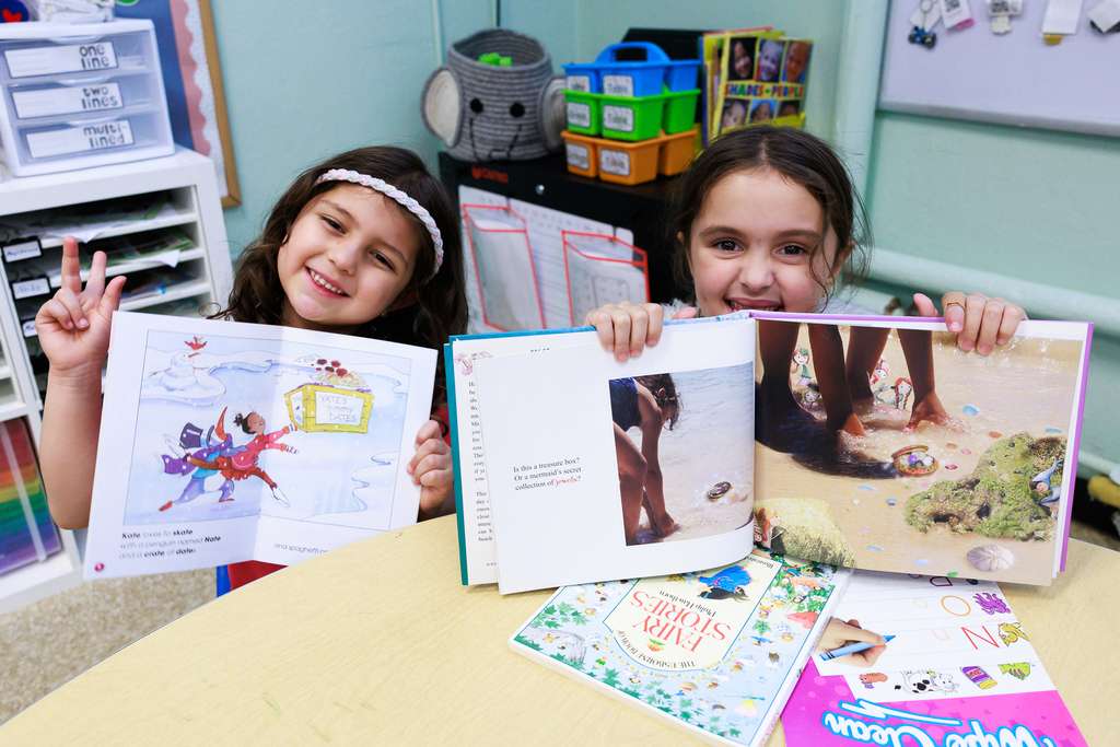 Two students sit side by side and proudly show off their books.