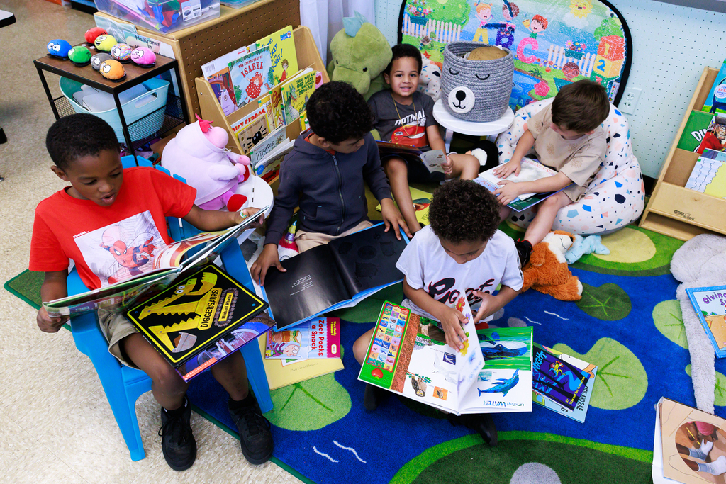 A group of students sit on the rug and are focused on reading.