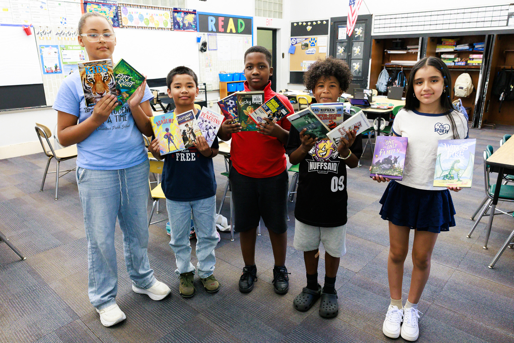 Five fifth grade students stand side by side holding up their newly aquired books.
