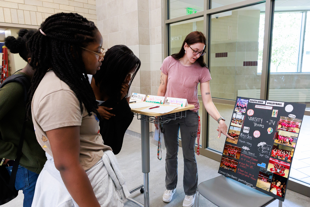 A teacher points to a posterboard with information about high school volleyball sign-ups.