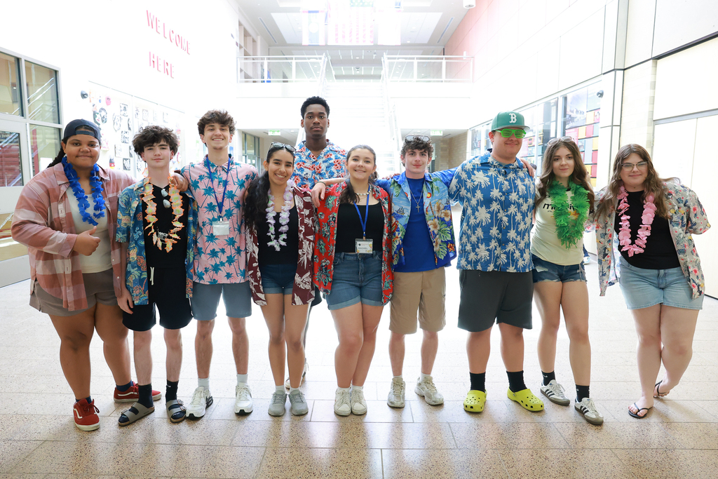 A group of 10 students stand together while wearing floral shirts following a summer musical performance.